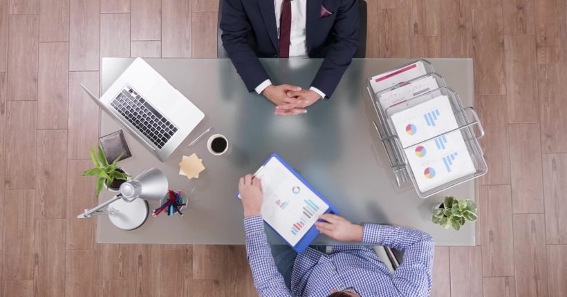 Top view of businessman analyzing financial documents discussing company strategy with partner during partnership meeting in startup office. Colleagues planning business strategy. Corporate agreement